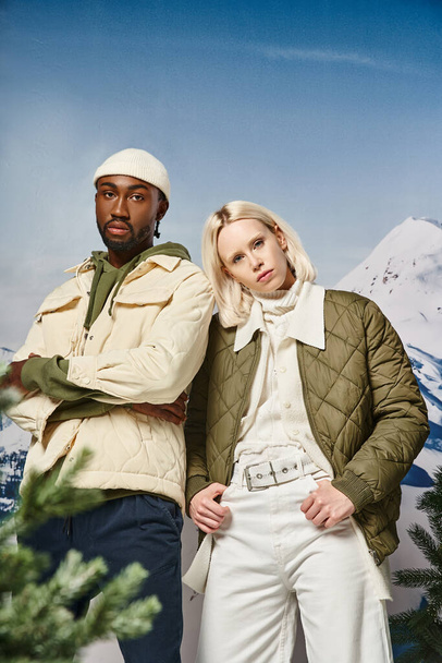 atractiva pareja en cálidas chaquetas de invierno posando juntos sobre fondo nevado, moda de invierno - Foto, imagen
