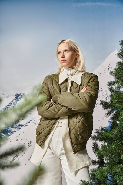 серьезная стильная женщина позирует со скрещенными руками на груди и смотрит в сторону, зимняя мода - Фото, изображение