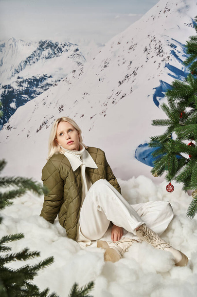 красива модна жінка в стильному вбранні, що сидить на снігу з схрещеними ногами, зимова концепція - Фото, зображення