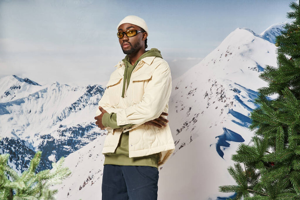 hombre afroamericano guapo en chaqueta blanca con brazos cruzados mirando a la cámara, moda de invierno - Foto, imagen