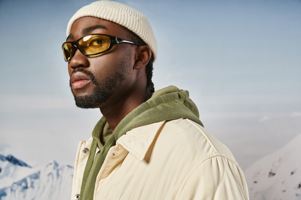 pohledný africký Američan muž v bílém čepici a sluneční brýle při pohledu na kameru, zimní móda - Fotografie, Obrázek