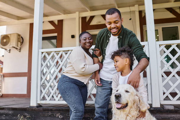 family photo, happy african american parents and son playing with dog on backyard of their house - Foto, afbeelding