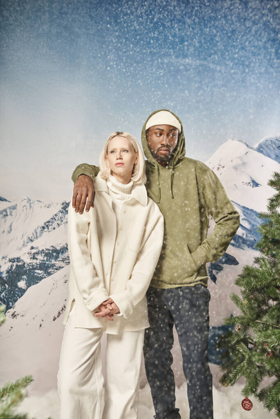 εμφανίσιμος άντρας με κομψό σακάκι που βάζει το χέρι του στον ώμο της κοπέλας του κάτω από χιονόπτωση, χειμώνας - Φωτογραφία, εικόνα