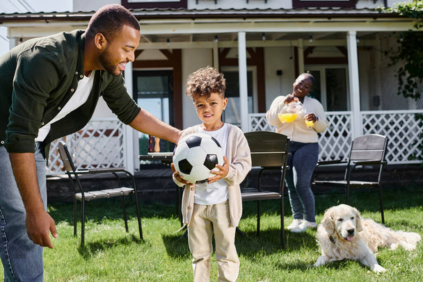 family weekend, happy african american father looking at son with soccer ball near wife on backyard - Φωτογραφία, εικόνα
