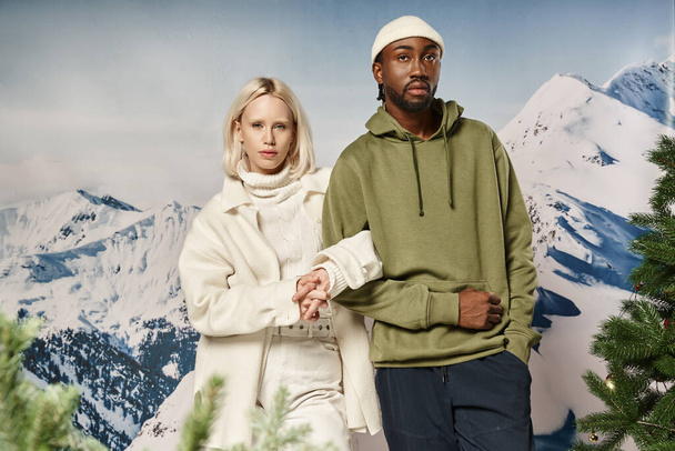 stylish blonde woman standing with african american boyfriend with mountain backdrop, winter fashion - Photo, Image