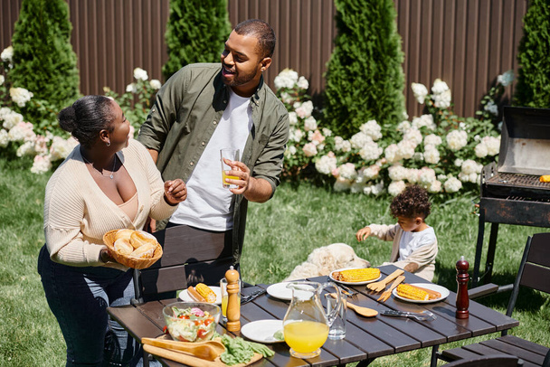 happy african american parents serving table in garden near son playing with dog on backyard - Photo, Image