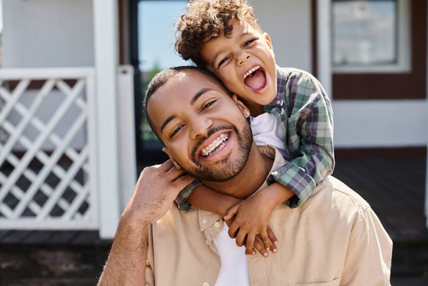 positive african american boy hugging excited father in braces on backyard of house, quality time - Фото, зображення