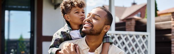 lindo afroamericano chico abrazando emocionado padre en aparatos ortopédicos en el patio trasero de la casa, bandera - Foto, imagen