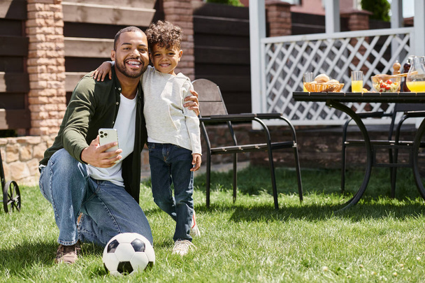 щасливий афроамериканський батько і син тримають смартфон, стоячи на задньому дворі будинку - Фото, зображення