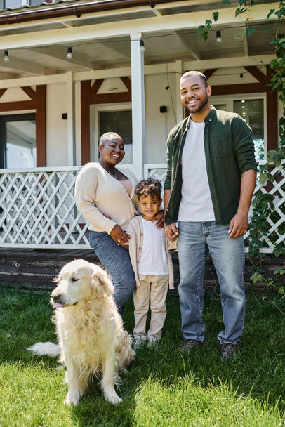 foto familiar, padres afroamericanos alegres e hijo sonriendo cerca lindo perro en el patio trasero de la casa - Foto, Imagen