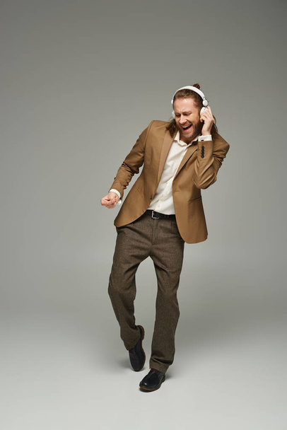 гарний бородатий бізнесмен в навушниках слухає музику на сірому фоні, танцює - Фото, зображення
