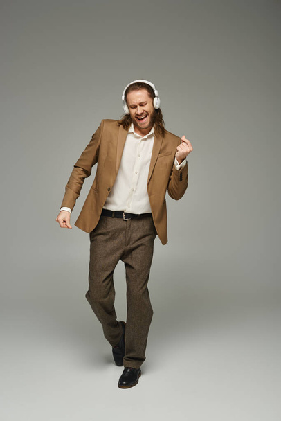 cheerful and bearded businessman in wireless headphones listening music on grey backdrop, dance - Photo, Image