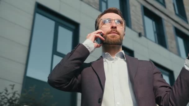 Bosszús kaukázusi férfi üzletember beszél mobiltelefon dühös nézd meg karóra ellenőrzés idő stressz késés üzleti találkozó határideje kívül iroda frusztrált munkáltató vár ügyfél a szabadban - Felvétel, videó