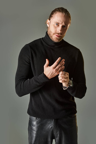 handsome bearded man in black turtleneck sweater wearing silver ring on finger on grey background - Foto, immagini