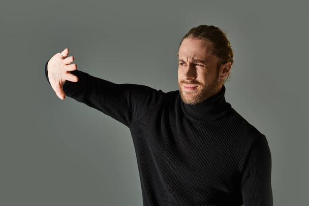 portrait of displeased man in turtleneck sweater posing with hands near face on grey backdrop - Photo, Image