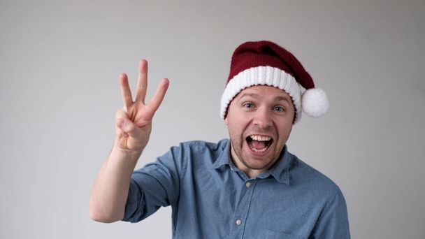 Hombre divertido en un año nuevo Sombrero cuenta los dedos, como muestra números. Captura de estudio - Foto, imagen