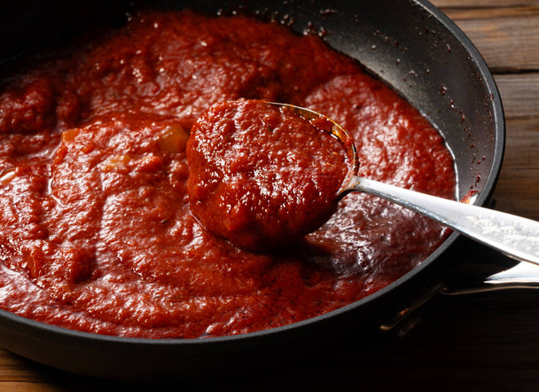Recoge la salsa de tomate en la sartén con una cuchara. Escena de cocina. Primer plano. Fondo de madera. - Foto, Imagen