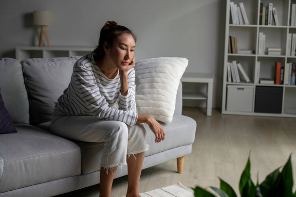  Одинокая азиатка в беде, обеспокоена, смущена, сидит дома на диване. Женщины страдают от психических расстройств. - Фото, изображение