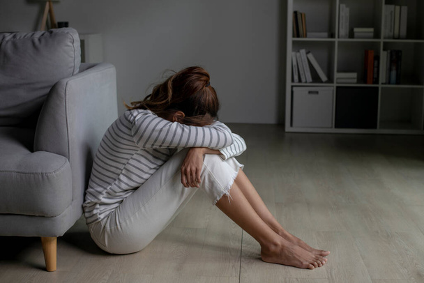 Junge Asiatin sitzt zu Hause auf dem Boden und fühlt sich traurig müde und besorgt und leidet unter Depressionen in psychischer Gesundheit.Frauen leiden unter psychischen Problemen. - Foto, Bild