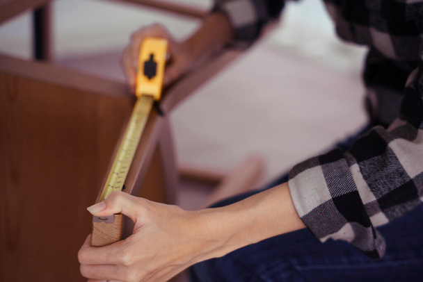 Kobiety mierzące długość krzesła taśmą pomiarową podczas montażu i renowacji mebli krzesełkowych. - Zdjęcie, obraz