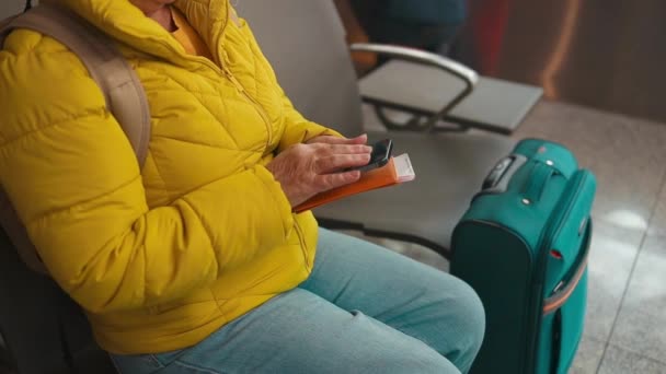 Primer plano de las manos caucásicas de la mujer en el aeropuerto revisando su teléfono inteligente mientras que la tarjeta de embarque espera el vuelo - Metraje, vídeo