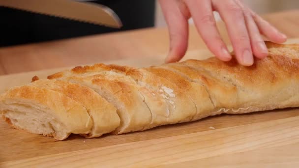 De handen van een meisje sneden een stokbrood op een houten plank met een broodmes. Close-up - Video