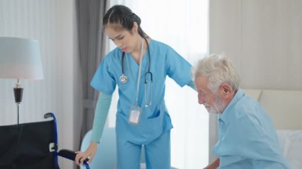 Eine Krankenschwester hilft einem älteren Mann, aus dem Bett aufzustehen. Pflegende Krankenschwester unterstützt Pflegebedürftige beim Aufstehen aus dem Bett und bei der Bewegung in Richtung Rollstuhl. Älteren behinderten Männern beim Aufstehen helfen. - Filmmaterial, Video