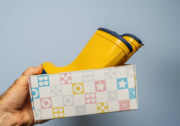 Ένα αρσενικό χέρι παρουσιάζει ένα σχολαστικά συσκευασμένο ζευγάρι κίτρινες μπότες σε ένα ουδέτερο γκρι φόντο - Φωτογραφία, εικόνα