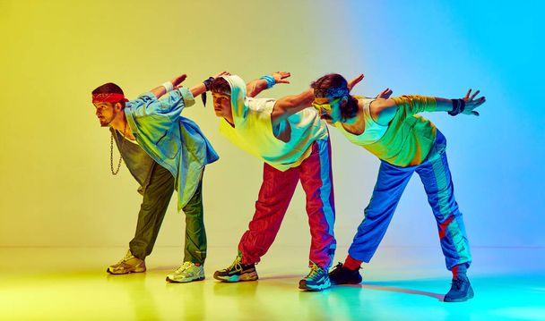 Stretching and warming up exercises. Stylish an in retro sportswear training against gradient yellow blue background in neon light. Concept of sportive and active lifestyle, humor, retro style. Ad - Fotoğraf, Görsel