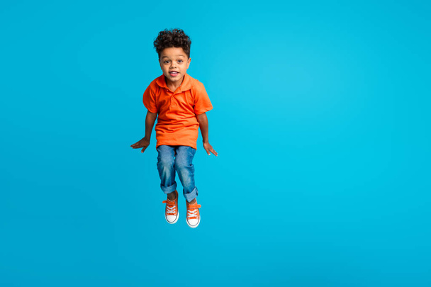 Full photo of jumping high trampoline funky schoolboy energetic overjoyed wear orange t shirt denim jeans isolated on blue color background. - Фото, изображение
