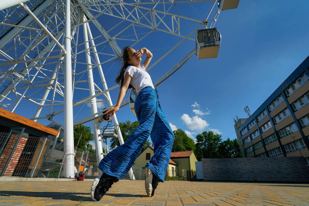 Foto al aire libre de joven adolescente caucásico de pie en los dedos de los pies con noria en el fondo en Zelenogradsk. - Foto, Imagen