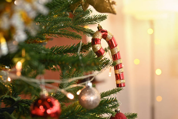 Christmas tree branch decorated with candy cane and baubles with blurred shiny lights on background. - Photo, Image