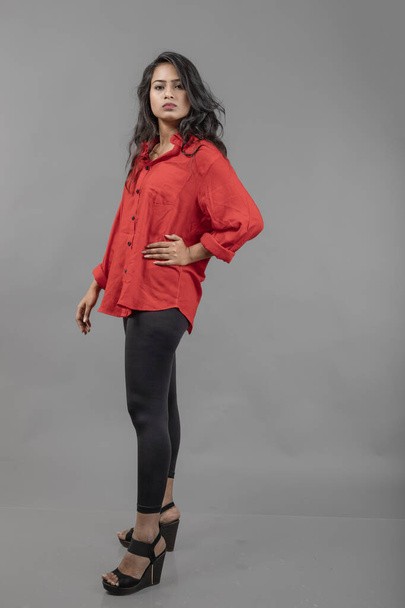 Ινδικό νεαρό θηλυκό μοντέλο σε casual φορούν σε γκρι φόντο - φωτογραφία αρχείου. Μακριά μαύρα μαλλιά μοντέλο φορώντας κόκκινο πουκάμισο και μαύρο τζιν. - Φωτογραφία, εικόνα