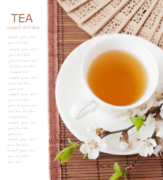 Tisana (colazione a base di tè con tazza di tè e fiori in fiore su tappetino di bambù isolato su bianco con testo campione
 ) - Foto, immagini