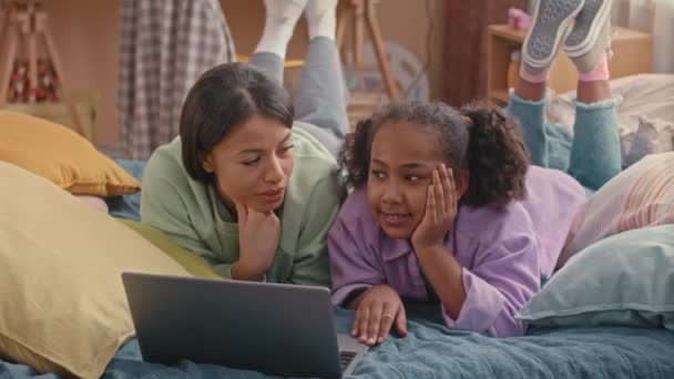 Afrika kökenli Amerikalı anne ve kız çocukları yumuşak yataklarında uzanmış, yatak odasında sohbet ediyor ve dizüstü bilgisayarda geziniyorlar. - Video, Çekim