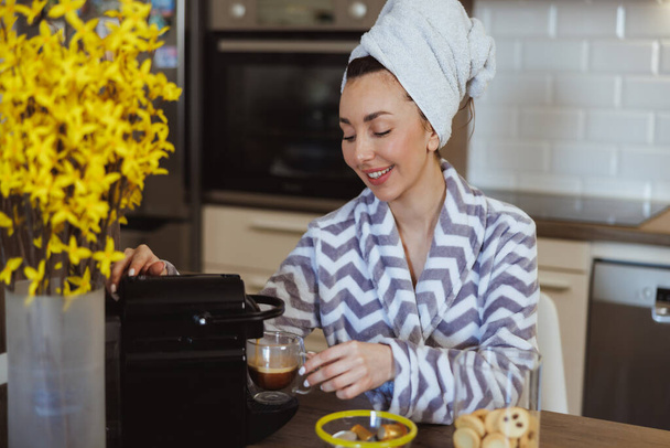 Jeune femme en peignoir faisant du café avec une machine à café sur la cuisine à la maison. - Photo, image