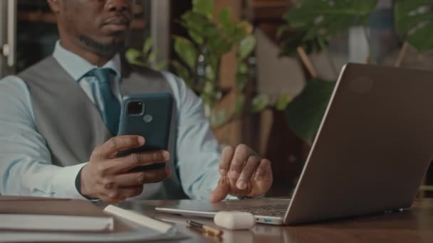 Pas se mladý africký americký podnikatel v klasickém formalwear pomocí smartphone a notebook při práci u stolu v restauraci - Záběry, video