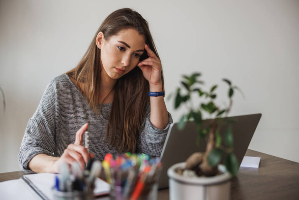 Jeune femme entrepreneure regardant réfléchi tout en travaillant à partir de son bureau à domicile. - Photo, image