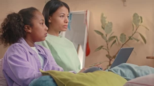 幸せな若いBiracialの女性と彼女の10歳の娘は,ラップトップとチャットで子供の寝室でベッドに座って,自宅で一緒にレジャー時間を過ごしています - 映像、動画