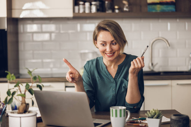 Idősebb női szabadúszó laptoppal videóhívást kezdeményez, miközben az otthoni irodájából dolgozik.. - Fotó, kép