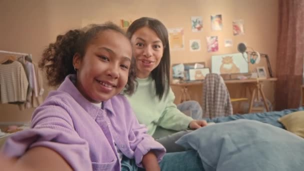 活気に満ちたキッズベッドルームでベッドに座って一緒にビデオブログを録画する母親とアフリカ系アメリカ人の少女のハンドヘルドPOV - 映像、動画