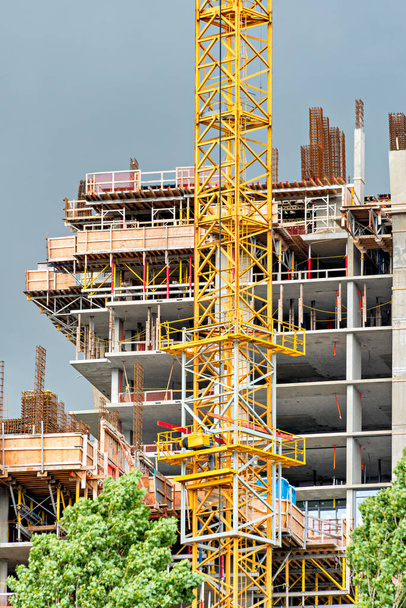 Výstavba vysoké betonové obytné budovy se žlutým jeřábem vpředu za bouřlivého počasí - Fotografie, Obrázek