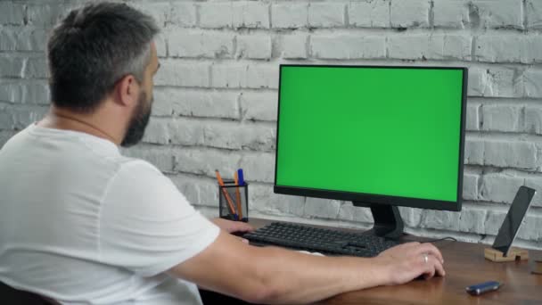 Barbudo hombre de mediana edad que trabaja en la computadora de escritorio con Green Mock Up Screen. Interior- Oficina moderna con pared de ladrillo blanco - Metraje, vídeo