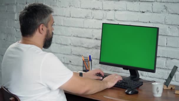 Barbudo hombre de mediana edad que trabaja en la computadora de escritorio con Green Mock Up Screen. Interior- Oficina moderna con pared de ladrillo blanco - Metraje, vídeo