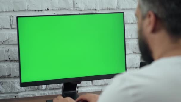 Uomo barbuto di mezza età che lavora al computer desktop con schermo verde finto. Interno- Ufficio moderno con muro di mattoni bianchi - Filmati, video