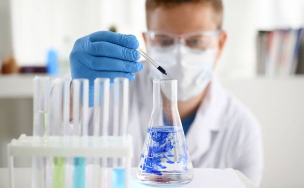 Erkek bir kimyager elinde cam test tüpü tutarak potasyum permanganatın sıvı çözeltisini taşır. Kimyasal imalat kullanan reaksiyonların su örneklerinin analizini yapar. - Fotoğraf, Görsel