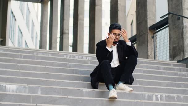 Nieszczęśliwy smutny indyjski biznes człowiek sfrustrowany stres pensive uczucie złe po bezrobociu firmy stracił problem z pracą rozwiązanie kryzysu na świeżym powietrzu. Arabian hinduski freelancer facet siedzi na schodach w centrum miasta - Materiał filmowy, wideo