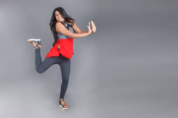 Prise de vue en studio d'une jeune et belle mannequin indienne en tenue décontractée portant un top design rouge et gris et un jean noir sur fond blanc. Modèle féminin. Portrait de mode. - Photo, image