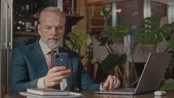 Pas se portrét elegantního zralého bělocha podnikatele v obleku při pohledu do kamery, zatímco sedí u stolu s notebookem, pracuje na dálku - Záběry, video