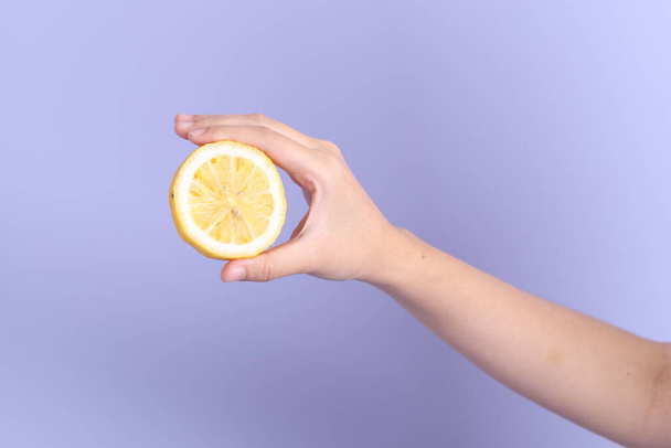 La donna asiatica mano che tiene il limone sullo sfondo viola. - Foto, immagini